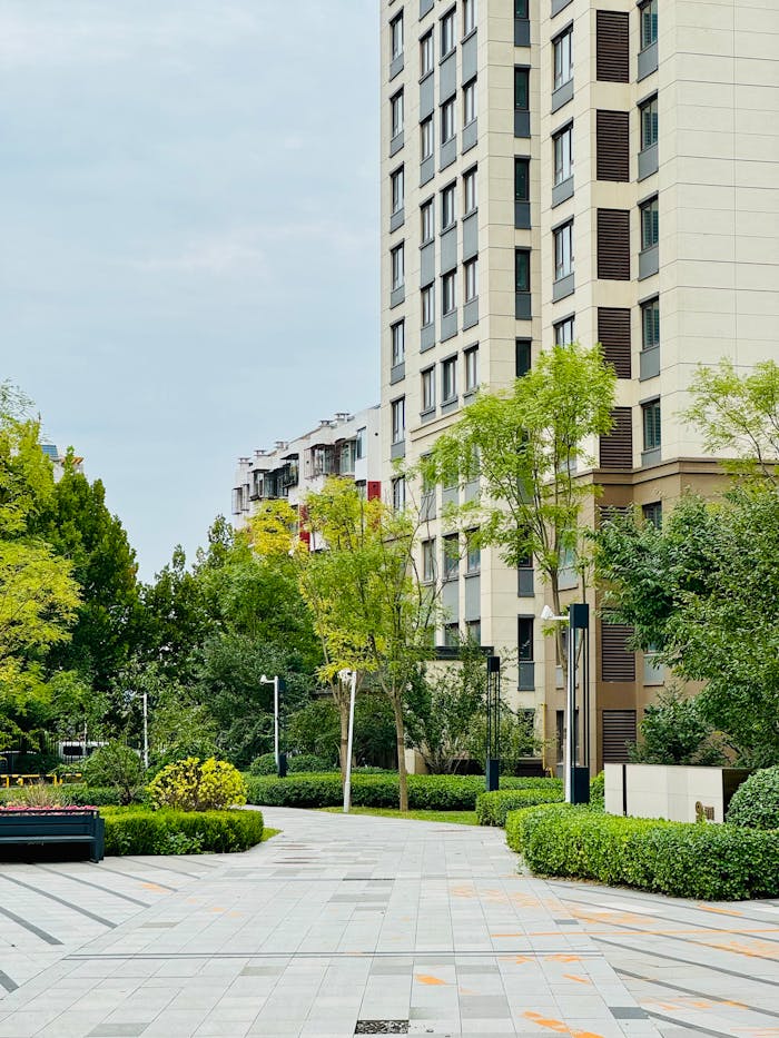 High-rise apartment buildings surrounded by lush green trees and landscaped pathways in a serene urban setting.