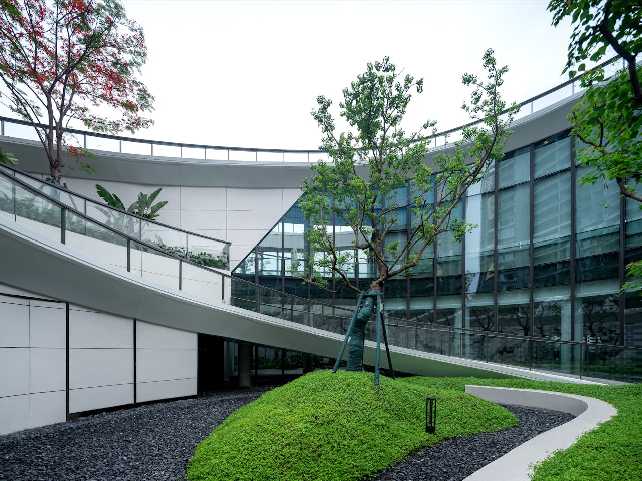 home-hero Curved glass building with lush green landscaping and modern design.